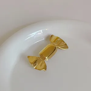 Macro shot of candy-shaped gold metal brooch with a reflective mirror finish on a ceramic plate