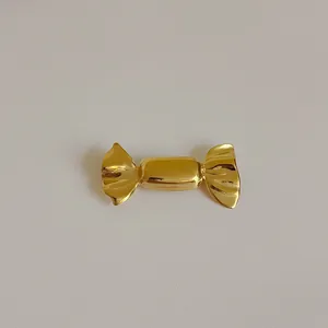 Macro shot of gold candy-shaped metal brooch showing high glossy finish and textures