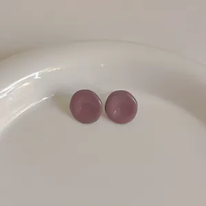 Detail von runden mauve Emaille-Ohrsteckern auf einem weißen Porzellanteller im minimalistischen Stil