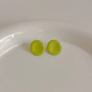 Nahaufnahme hellgrüner runder Ohrstecker mit glänzender Emaille auf einem Keramiktablett