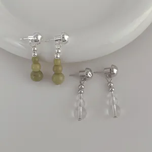 Detailed close-up of avocado green stone and clear crystal beaded tassel earrings on ceramic