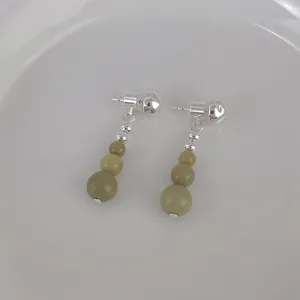 Macro detail of avocado green stone beaded tassel earrings on a ceramic dish
