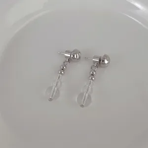 Close-up of silver beaded drop earrings with transparent beads on white ceramic tray