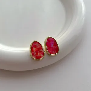 Detailaufnahme roter Acryl-Ohrringe mit goldenem Metallrand auf einem Keramiktablett