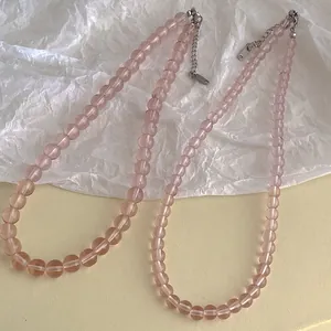 Pink glass beaded necklace with silver lobster clasp on a textured white background