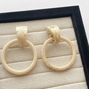 Detail van beige marmeren hars oorringen gepresenteerd in een stoffen sieradendoosje