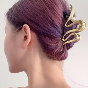 Eleganter mattgoldener gewellter Metall-Haarclip mit Perle auf lila Haaren