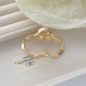 Détail d'une pince à cheveux dorée ondulée irrégulière avec un design en métal creux