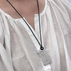 Minimalistische silberne Kamm-Halskette mit schwarzer Kordel auf weißer Bluse