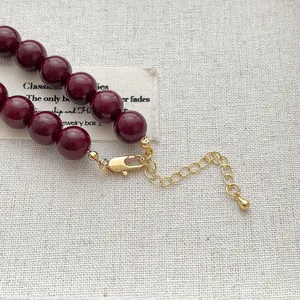 Elegante tiefrote Perlenkette mit goldenem Karabinerverschluss auf weißem Stoffhintergrund