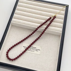 Nahaufnahme der dunkelroten Perlenkette mit goldenem Karabinerverschluss auf Leinentablett