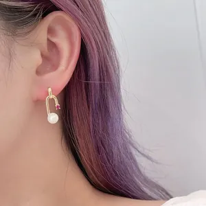 Detail shot of a U-shaped gold earring with white pearl and red stone worn by a model