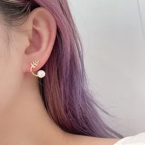Close-up of golden leaf design earring with white freshwater pearl worn by a model