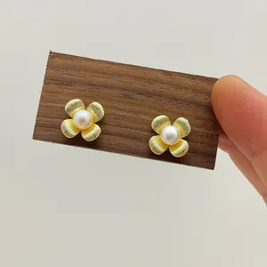 Detail of floral earrings with brushed gold petals and a white freshwater pearl center
