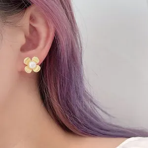 Close-up of golden flower stud earrings with pearl centers worn on ear by model