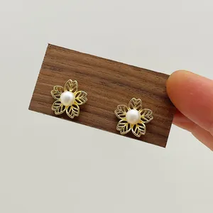 Close-up of gold hollow flower earrings with natural pearls on a wooden display
