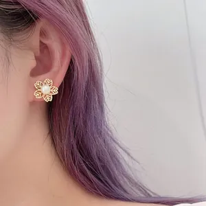 Close-up of a model wearing elegant gold floral pearl earrings with hollow petal design