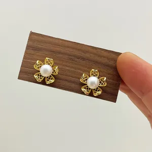 Close-up of gold flower earrings with a pearl center on a wooden display card