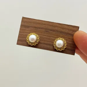 Detail of freshwater pearl stud earrings with ornate gold hollow floral base on wood stand