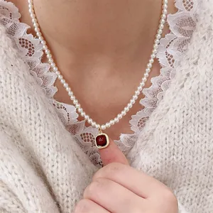 Close-up of pearl necklace with red agate square pendant worn on a model neck