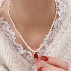 Close-up of pearl necklace with red oval pendant and gold frame on lace collar