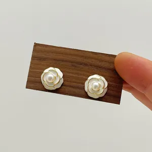 Macro view of camellia pearl earrings featuring white enamel petals and gold base