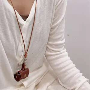 Mini brown leather necklace pouch for earphones with metal buckle detail on white shirt