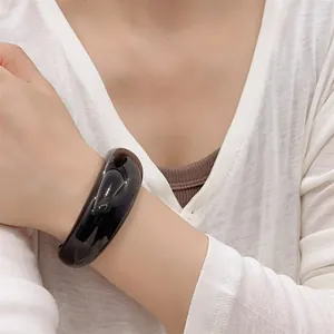 Close-up of wide chunky black resin bangle bracelet with a high-gloss polished finish