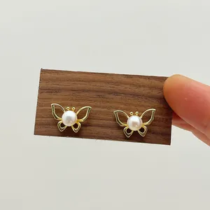 Detailed close-up of hollow butterfly earrings in gold finish with freshwater pearl center