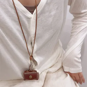 Detailed view of mini brown leather coin purse necklace worn over a white cardigan