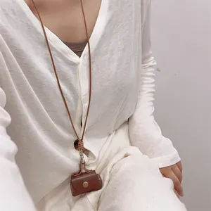 Detail of a brown leather mini pouch necklace with metallic snap button on white knitwear