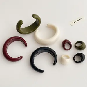 Close-up of minimalist resin bangles and thick rings in green, cream, red, and black