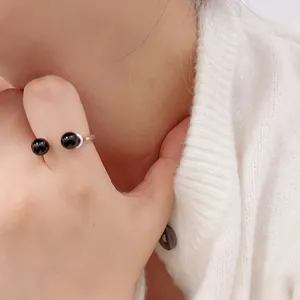 Close-up of a silver open ring featuring two polished black onyx beads on a hand
