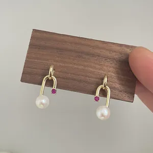 Detailed macro view of gold U-shaped earrings with white freshwater pearl and purple gemstone