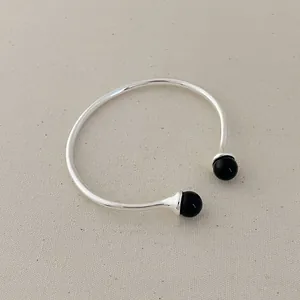 Detail of silver open bangle featuring dual black spherical beads on a textured background