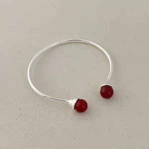 Detailed close-up of open cuff bracelet with red agate beads on textured fabric