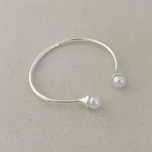 Detailed close-up of a silver metal open bangle with white pearls on a linen fabric