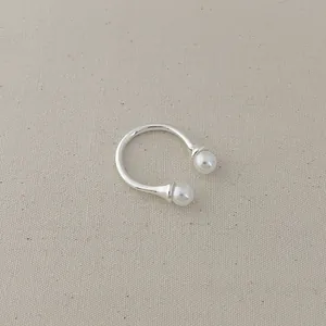 Close-up of a silver open ring featuring two white pearls on a soft beige fabric background