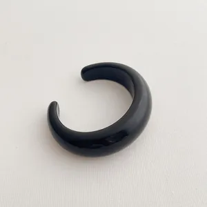 Detail view of a minimalist black resin C-shaped open cuff bracelet with glossy finish
