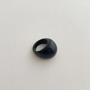 Chunky minimalist black resin ring with a glossy finish on a textured white background