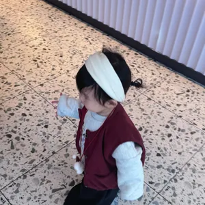 Detailed look at burgundy knit baby vest paired with cream long-sleeve shirt and headband