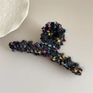 Primer plano de pinza de pelo de felpa negra con pompones de colores e hilos dorados