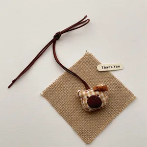 Detail of a handmade brown bear charm with yellow checkered fabric and a brown bow tie