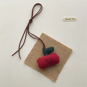 Detailed view of handmade red fabric cherry pendant with black embroidery and cotton cord