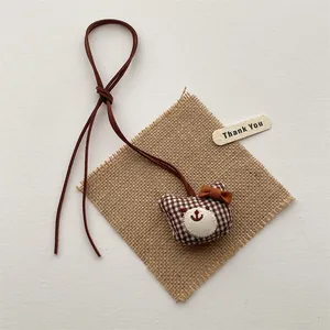Detailed view of a brown plaid fabric teddy bear pendant with a caramel bow tie and leather cord
