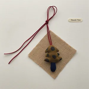 Handmade green polka dot plush forest tree pendant with red lanyard on linen mat