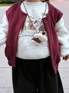 Detail of red corduroy vest and white sweatshirt with cute puppy print and duck pendant