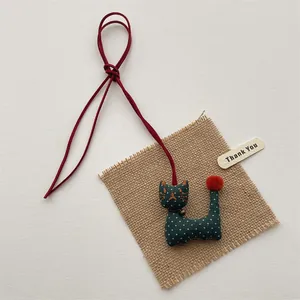 Detail of handmade green fabric cat charm with orange pompom and gold bell accessory
