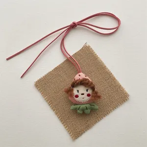 Detail of a handmade plush strawberry girl doll pendant with a pink suede bow lanyard