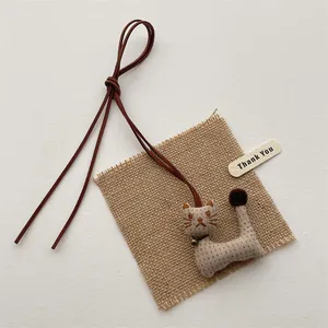 Close-up of handmade cloth cat pendant with leather cord and gold bell on rustic burlap